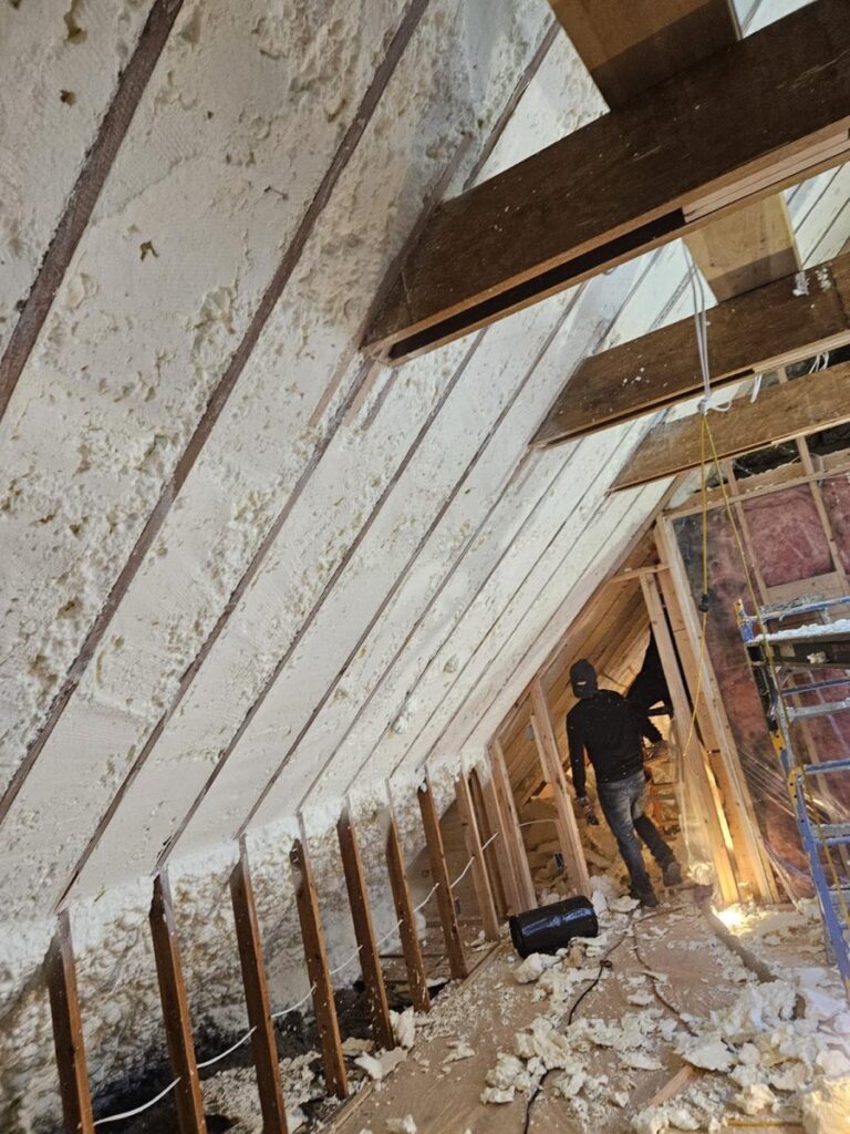 Our crew spraying foam along an attic roofline after removing old fiberglass