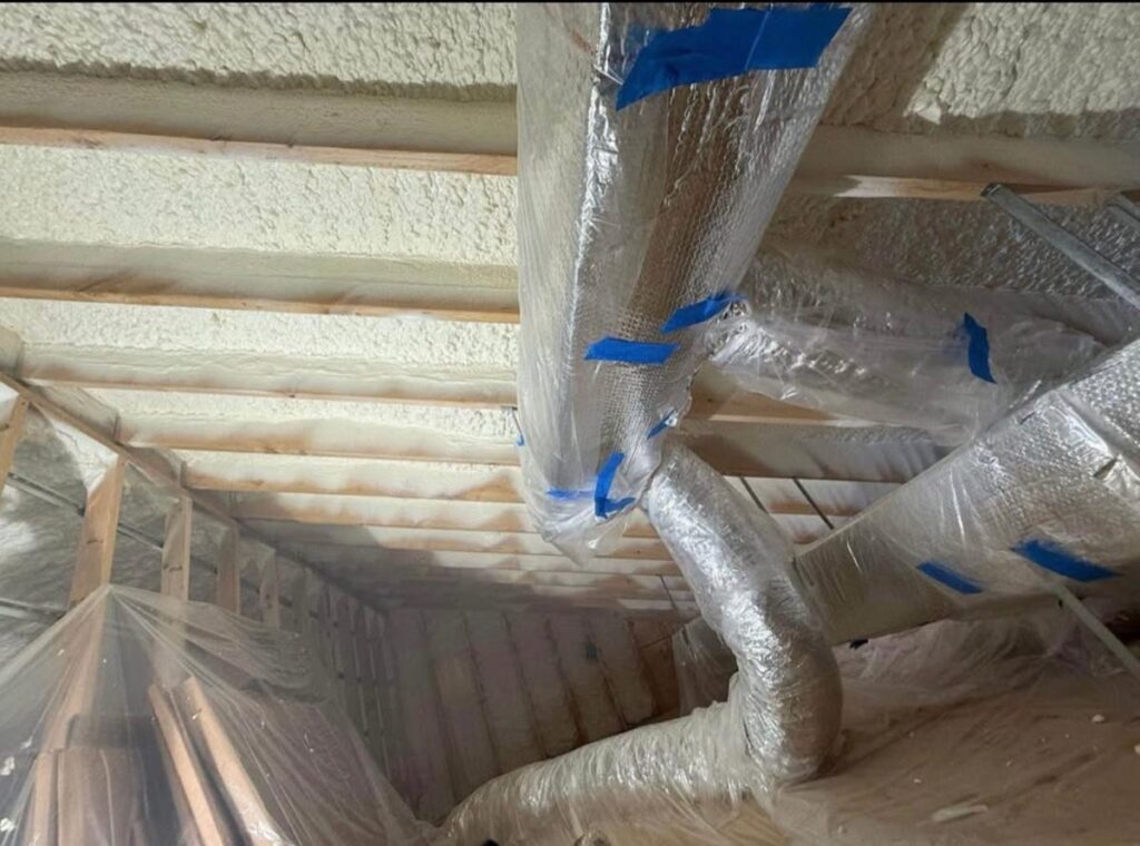 Ductwork wrapped and taped off before spray foam is applied in an attic