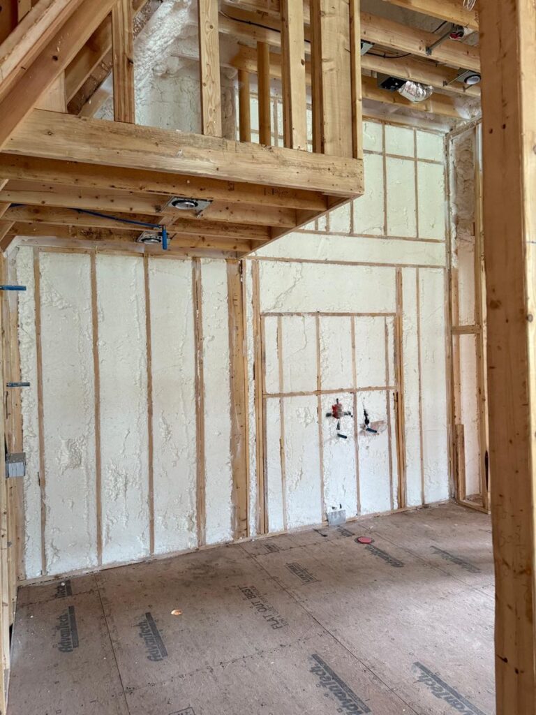 Spray foam filling interior wall cavities around a plumbing rough-in